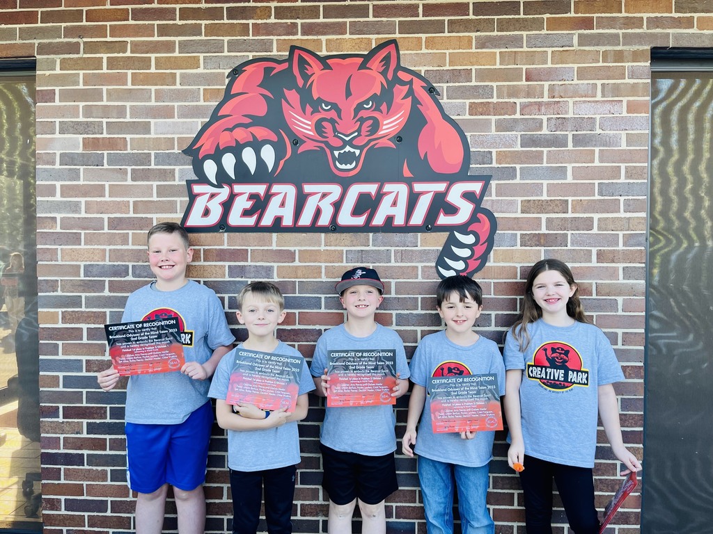 group of 5 children posing in front of bearcat sign